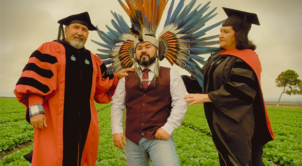 Eric Becerra (center) wears his Aztec dancer headdress, while his parents don the doctoral regalia.