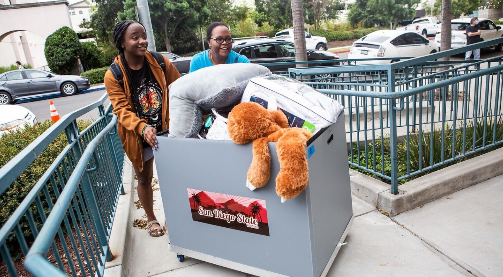 Photograph of a family rolling a cart filled with a student's belongings on SDSU Move-In Day.