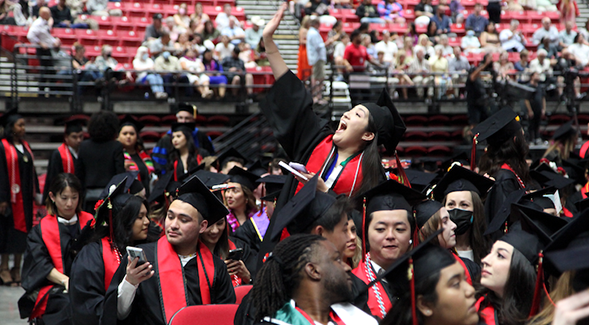 An SDSU graduate waves into the crowd at Viejas Arena during the university's 2022 commencement ceremony. (SDSU)