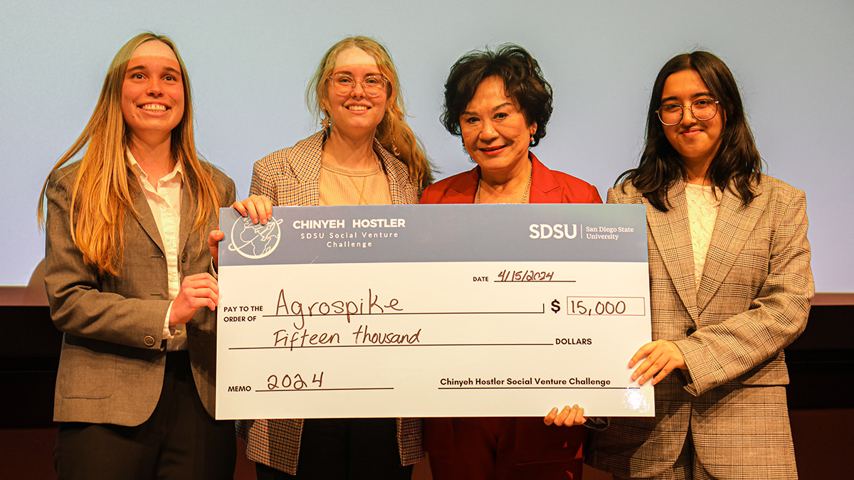 Three students in businesswear and sponsor Chinyeh Hostler posed with a novelty check for $15,000 from the Chinyeh Hostler Social Venture Challenge, dated April 15, 2024, and made out to "Agrospike."