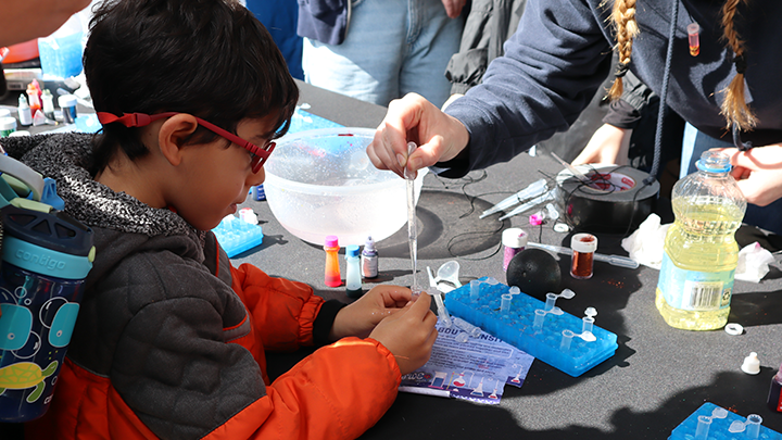 A young student participates in a mini lava lamp necklace activity during the 2024 STEM Festival at Snapdragon Stadium.