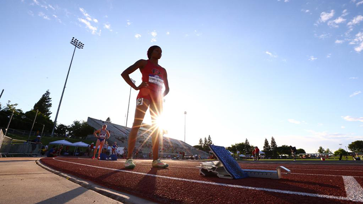 SDSU sprinter Sydney Bentley stands on the race track preparing for a race as the sun sets behind her. 