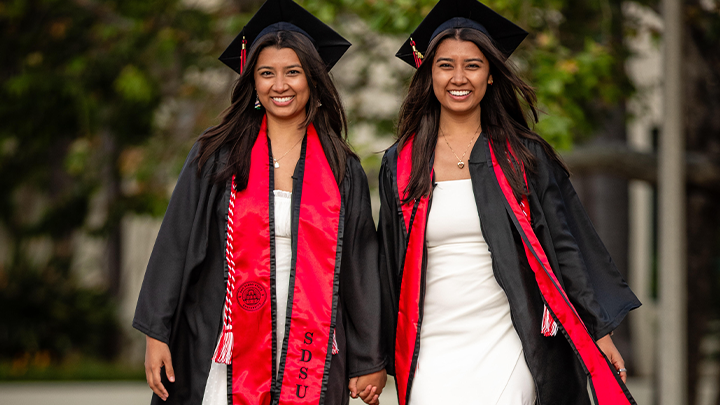 Image of Sabrina and Sydney Moreno in their cap gowns walking through the SDSU campus.
