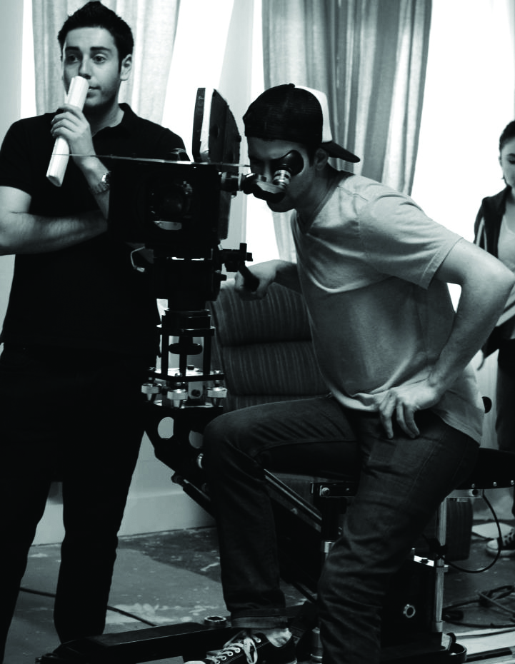 2 people on set, one is looking through the lens of a camera