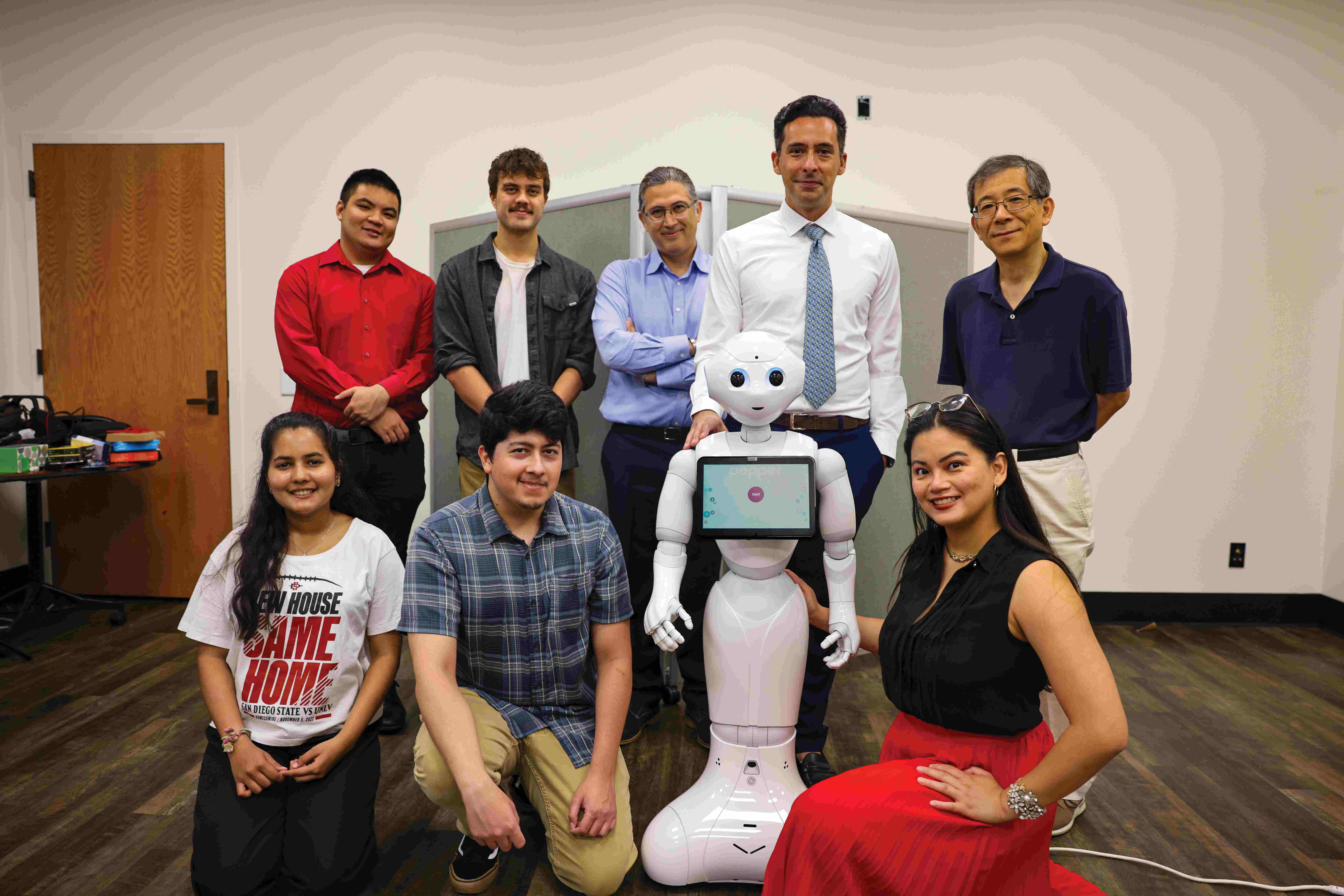 A group of students and staff posing with Pepper