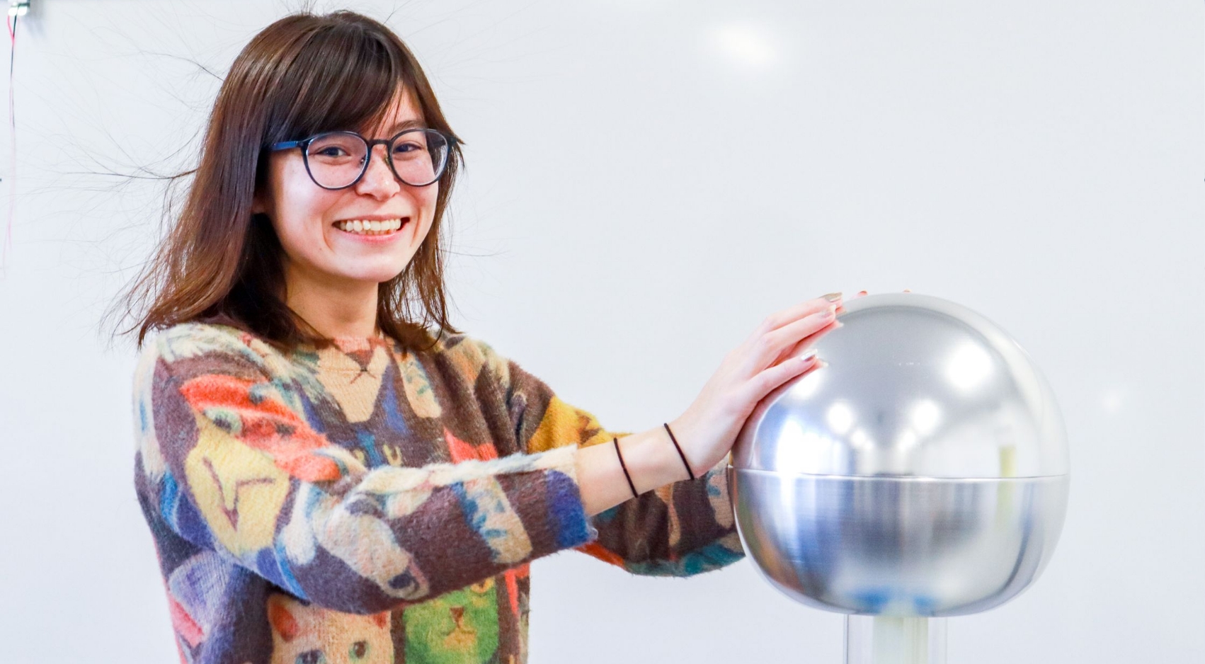 Ngara Birds hair stands on end while she touches a Van de Graaff generator.