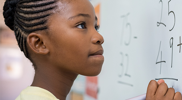 A young student stands at a white board and works on a math problem. (Adobe Stock)