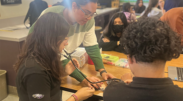 Instructor is leaning over table helping students sitting around said table