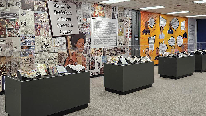 Image shows a wall mural and the exhibit 'The Rising Up: Depictions of Social Protest in Comics' in the SDSU University Library Special Collections area.