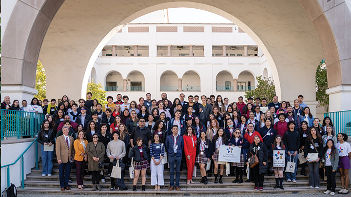 Image shows visiting high school students and teachers posing for a photo under the Conrad Prebys Aztec Student Union arch at SDSU.