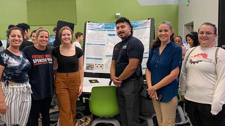 SDSU students pose at a table with their presentation boards detailing their research.