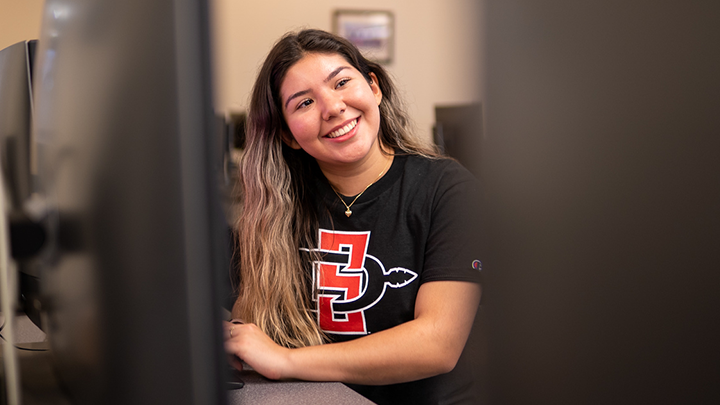 Girl wearing SDSU shirt sits at computer