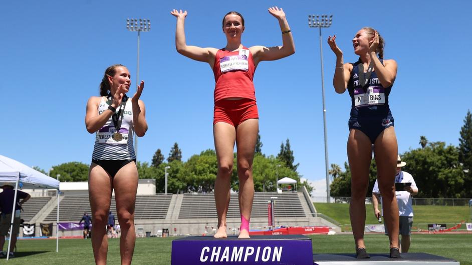 Gold medalist Jenna Fee Feyerabend raises her arms in celebration at the top of finisher's podium.