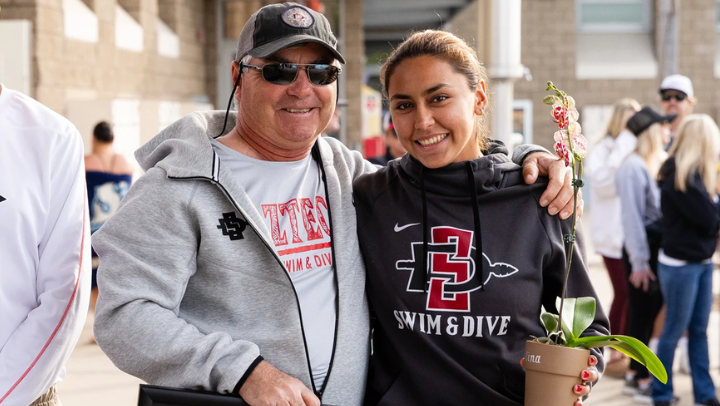 A poolside photo of SDSU dive coach Roland McDonald and student-athlete Valentina Lopez Arevalo smiling during Senior Day.