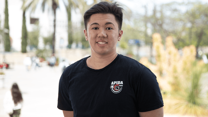 Ethan Quinn, wearing a black shirt with the APIDA organization logo, poses for a photograph while on campus at SDSU.