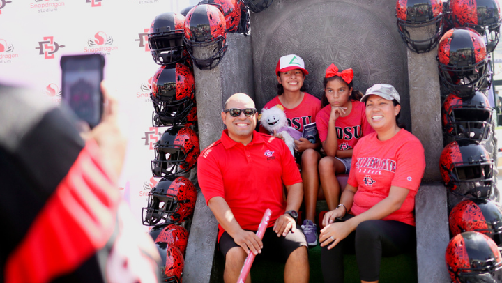 SDSU fans sit on a throne framed by football helmets during a familly photo at Fan Fest 