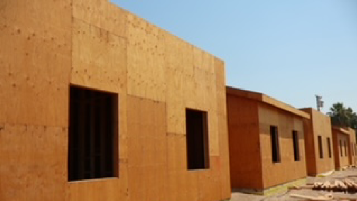 The woodframe exterior of a construction project of four one-story buildings, with openings where the windows will be installed, and a short pile of lumber on the ground.