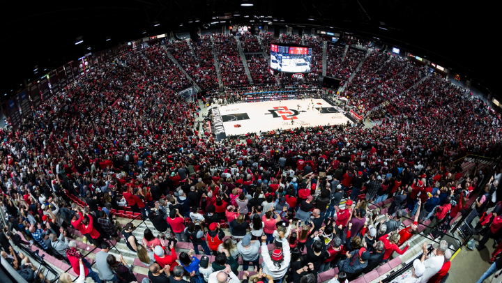 Bird's eye view of inside a crowded Viejas Arena during a men's basketball game shows fans cheering from their seats.
