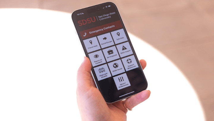 A student holding a cell phone displaying the SDSU Ready app.