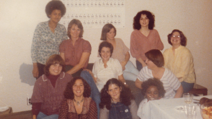 11 woman standing in 2 rows smiling